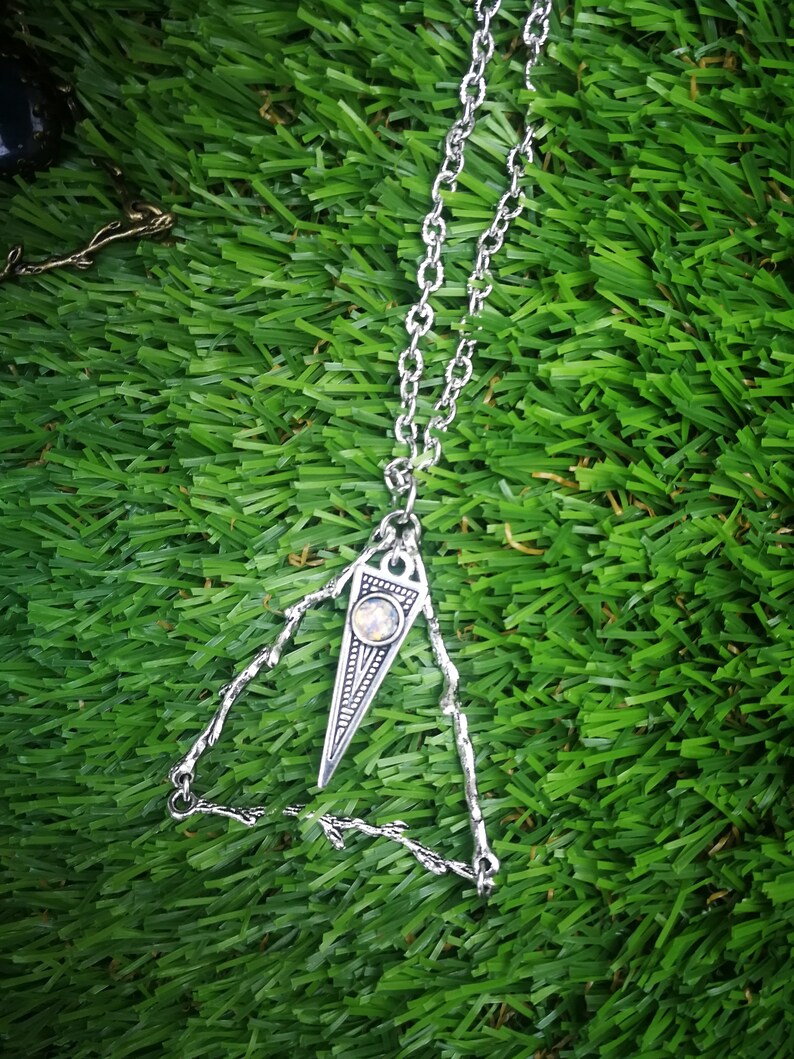 May include: A silver necklace with a triangular pendant featuring a clear gemstone. The pendant is made of intricate metalwork and has a delicate, bohemian style.