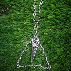 May include: A silver necklace with a triangular pendant featuring a small iridescent gemstone. The pendant is surrounded by a delicate, intricate silver design.