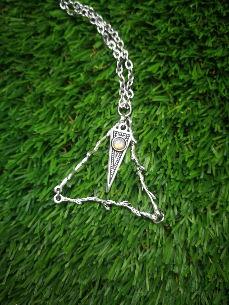 May include: A silver necklace with a triangular pendant featuring a small, round, yellow gemstone. The pendant is made of twisted wire and has a delicate, intricate design.