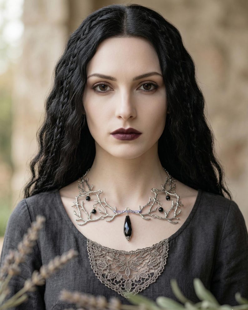 May include: A silver-toned necklace with a branch-like design, featuring black gemstone accents and a teardrop-shaped pendant. The necklace is worn over a gray dress with a lace neckline, creating a gothic or fantasy aesthetic.