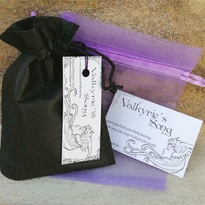 May include: A black drawstring bag with a white tag that says "Valkyrie's Song" and a purple organza bag with a white tag that says "Valkyrie's Song". The tags feature a black and white illustration of a woman with flowing hair and wings.
