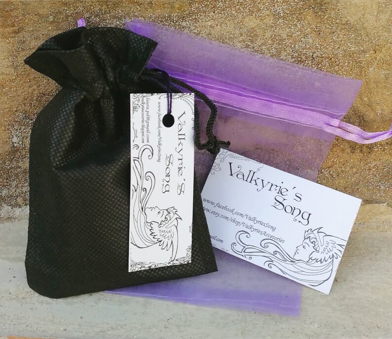 May include: A black drawstring bag with a white tag that says "Valkyrie's Song" and a purple organza bag with a white tag that says "Valkyrie's Song". The tags feature a black and white illustration of a woman with flowing hair and wings.