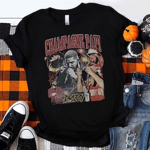 May include: Black t-shirt with a vintage-style graphic of a rapper, featuring the text "Champagne Papi" and "Drizzy".