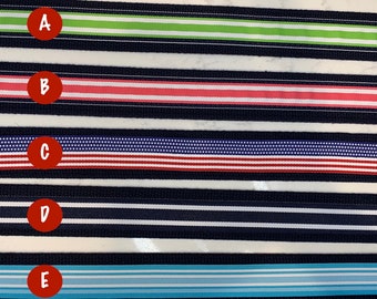 May include: Five different striped fabric ribbon samples. The ribbons are navy blue with white stripes. The stripes are different colors and patterns: green, pink, red with white stars, white, and blue.