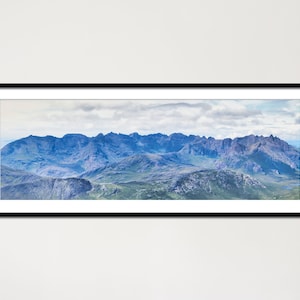 Könnte beinhalten: Gerahmter Panorama-Druck eines Gebirges unter einem bewölkten Himmel. Die Berge weisen Blau- und Grüntöne auf, mit zerklüfteten Gipfeln und Tälern. Der Rahmen ist schwarz, und der Druck ist vor einem weißen Hintergrund.