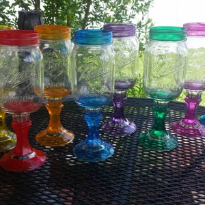 May include: A set of ten colorful mason jar glasses with painted stems. The glasses are arranged in a rainbow pattern on a black metal table.