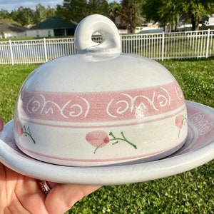May include: White ceramic butter dish with a pink and green floral design. The dish has a domed lid with a handle.