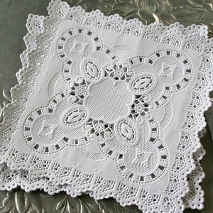 May include: White paper doilies with a delicate lace pattern. The doilies are square shaped and have a scalloped edge.