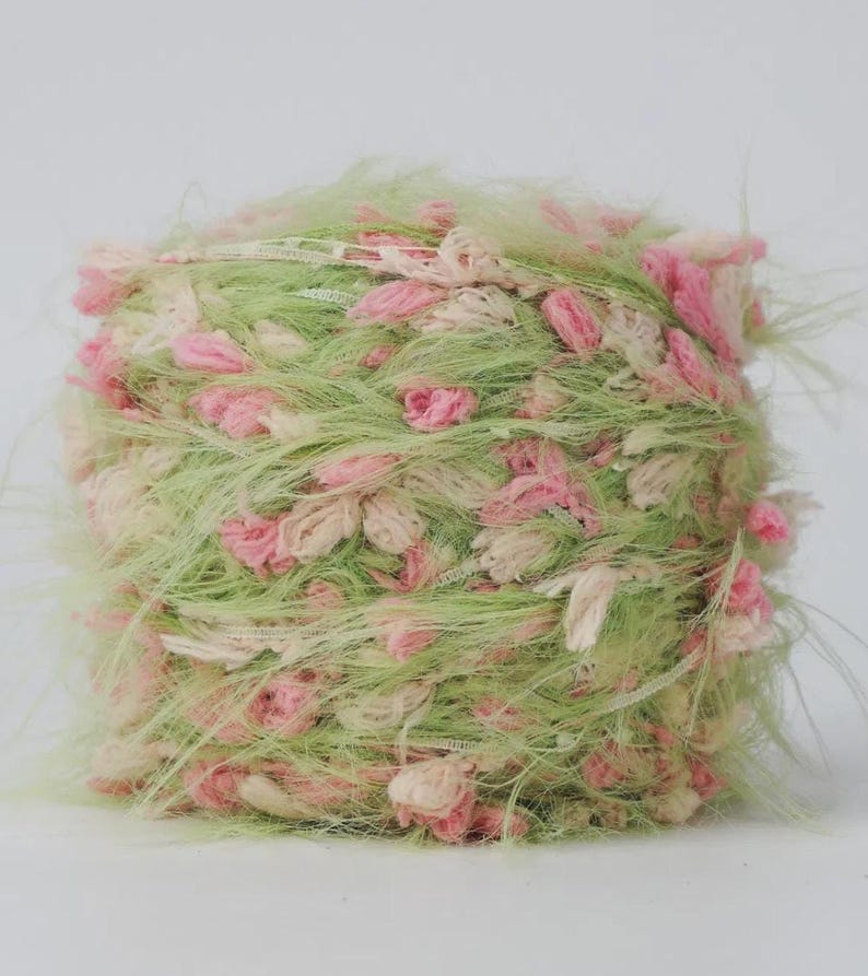Pode incluir: Novel de fio texturizado em tons de verde claro, rosa e creme. O fio tem uma apar&ecirc;ncia fofa e difusa com pequenos detalhes em forma de flor. Ideal para projetos de tric&ocirc; ou croch&ecirc;.