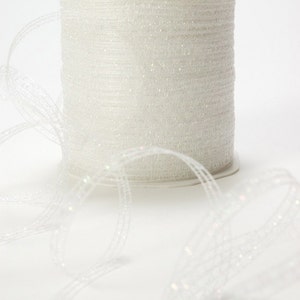 May include: A spool of white iridescent ribbon with a shimmery finish. The ribbon is unraveled and laying on a white surface.
