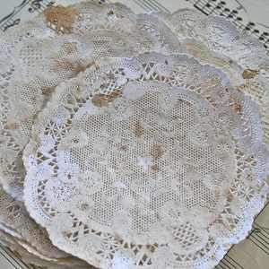 May include: A stack of white paper doilies with a delicate lace pattern. The doilies are slightly worn and have a vintage aesthetic.