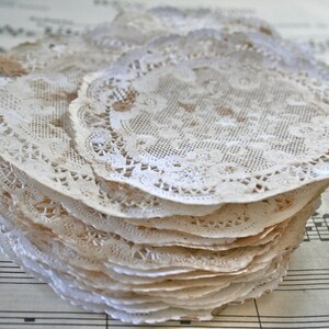 May include: A stack of delicate, off-white lace doilies with intricate floral patterns. The doilies are arranged in a circular pattern and have a slightly aged, vintage look.