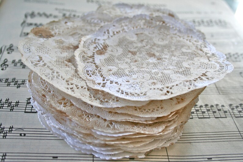 May include: A stack of delicate, off-white lace doilies with intricate floral patterns. The doilies are arranged in a circular pattern and have a slightly aged, vintage look.