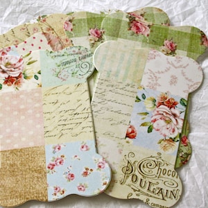 May include: A set of six vintage-style fabric scraps, each with a different pattern and design. The scraps are in shades of pink, blue, green, and white, and feature floral patterns, handwritten text, and polka dots. The scraps are shaped like a bone and are perfect for crafting projects.