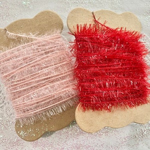 May include: Two spools of sparkly, fluffy trim. One spool is pink and the other is red. The trim is wrapped around cardboard spools.