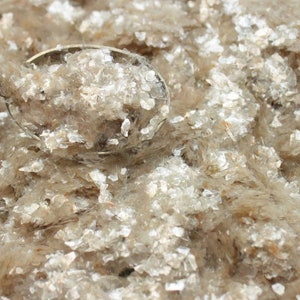 Peut inclure: Gros plan d'une cuill&egrave;re remplie de paillettes de mica. Les paillettes sont de couleur brun clair et ont une finition chatoyante et iris&eacute;e.