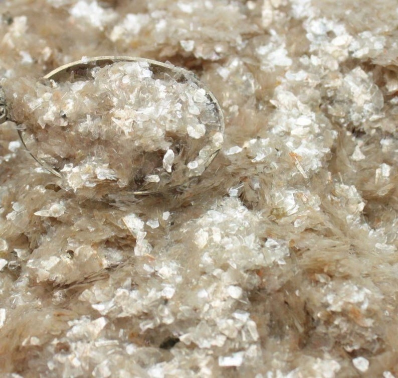 Peut inclure: Gros plan d'une cuill&egrave;re remplie de paillettes de mica. Les paillettes sont de couleur brun clair et ont une finition chatoyante et iris&eacute;e.
