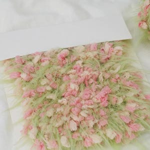 Pode incluir: Close-up de uma amostra t&ecirc;xtil com fibras rosa, creme e verdes. A textura parece fofa e em camadas, com fios curtos e longos. A paleta de cores &eacute; suave e pastel.