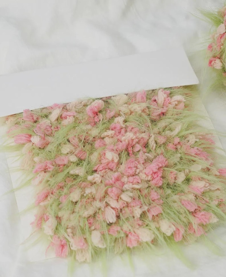 Pode incluir: Close-up de uma amostra t&ecirc;xtil com fibras rosa, creme e verdes. A textura parece fofa e em camadas, com fios curtos e longos. A paleta de cores &eacute; suave e pastel.