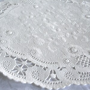 K&ouml;nnte beinhalten: Wei&szlig;e Papier-Deko-Serviette mit einem zarten Blumenmuster. Die Serviette hat einen gewellten Rand und ist perfekt, um jeder Tischdekoration einen Hauch von Eleganz zu verleihen.