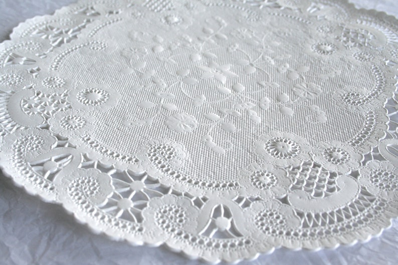 K&ouml;nnte beinhalten: Wei&szlig;e Papier-Deko-Serviette mit einem zarten Blumenmuster. Die Serviette hat einen gewellten Rand und ist perfekt, um jeder Tischdekoration einen Hauch von Eleganz zu verleihen.