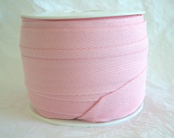 May include: A spool of pink cotton twill tape. The tape is woven with a herringbone pattern.