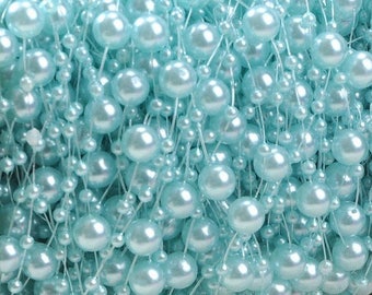 Puede incluir: Primer plano de una larga hebra de cuentas de perlas de color azul claro. Las cuentas están enhebradas en un alambre transparente y están dispuestas en un patrón aleatorio. Las cuentas son todas del mismo tamaño y tienen un ligero brillo iridiscente.