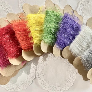 May include: A rainbow assortment of decorative yarn spools. Each spool is a different color, including pink, red, orange, yellow, green, purple, white, gray, and black. The yarn is displayed on heart-shaped cardboard holders.