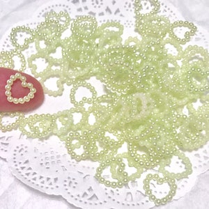 May include: A large quantity of small, pale green pearl heart-shaped embellishments. The embellishments are made of plastic and are perfect for adding a touch of sparkle to crafts and jewelry.