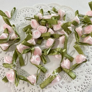 May include: A collection of pink and green fabric flower embellishments. The flowers are made of satin ribbon and have a delicate, vintage look.