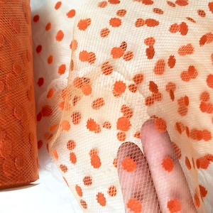 May include: Orange tulle fabric with a polka dot pattern. The dots are a slightly darker shade of orange.