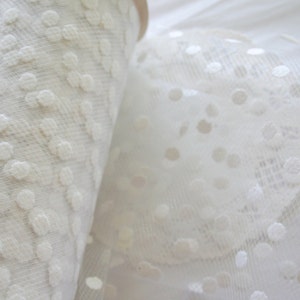 May include: Two rolls of white tulle fabric with a polka dot pattern. The fabric is sheer and delicate, with a soft, white color.