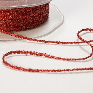 May include: A spool of red metallic thread with a glittery finish. The thread is wound around a clear plastic spool.