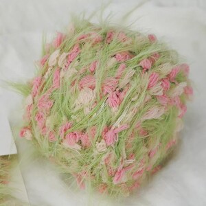 Pode incluir: Novel de fio texturizado em tons pastel de verde, rosa e creme. O fio tem uma apar&ecirc;ncia fofa e difusa com tufos de rosa e creme. Adequado para projetos de tric&ocirc; ou croch&ecirc;, adicionando textura e cor.