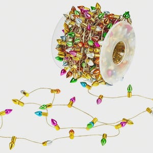 May include: A spool of colorful Christmas lights with gold wiring. The lights are shaped like teardrops and come in various colors, including gold, silver, pink, green, and blue. The lights are on a clear plastic spool.