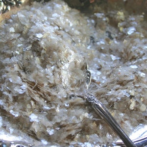 Peut inclure: Un plat de service en argent rempli de paillettes de mica iris&eacute;es. Une cuill&egrave;re en argent repose sur les paillettes.