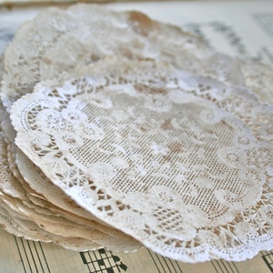 May include: A stack of white paper doilies with a delicate lace pattern. The doilies are arranged in a fan shape and have a slightly aged appearance.