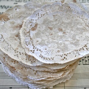 May include: A stack of white lace doilies with a delicate floral pattern. The doilies are slightly brown with age and are arranged on a sheet of music.