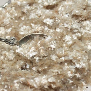 Peut inclure: Gros plan sur un tas de paillettes de mica, un mat&eacute;riau chatoyant et iris&eacute; souvent utilis&eacute; dans l'artisanat et les cosm&eacute;tiques. Les paillettes sont de couleur beige clair avec un reflet argent&eacute;.