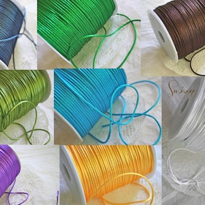 May include: Spools of colorful satin cord in various colors, including blue, green, brown, white, purple, and yellow. The cords are wound around white spools.
