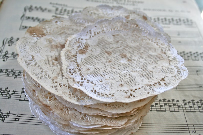 May include: A stack of white lace doilies with a delicate floral pattern. The doilies are arranged on a sheet of music.