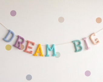 May include: A white wall with pastel coloured polka dots and a felt banner that reads "DREAM BIG". Two framed prints are hanging on the wall, one with a white rabbit and the other with a white dove with the text "Peace on Earth".