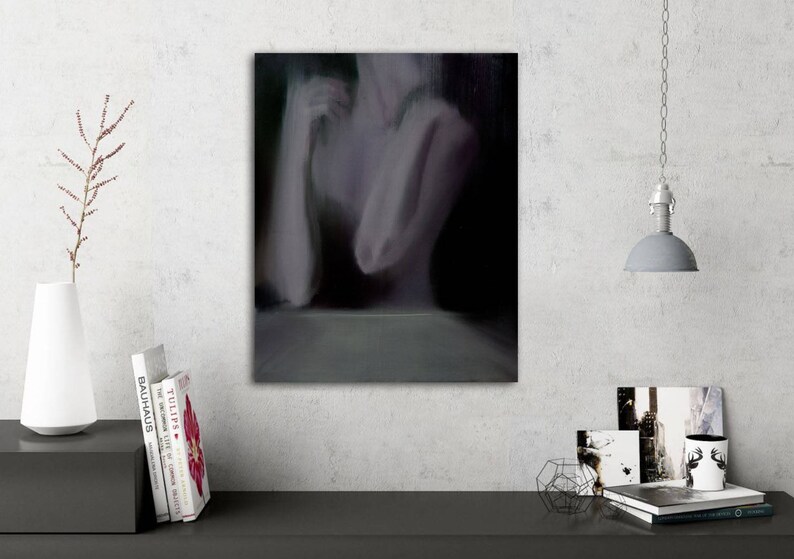 May include: An abstract painting on canvas depicts a blurred figure in shades of gray and purple. The artwork is mounted on a white wall, with a minimalist white vase, books, and a hanging lamp in the scene.