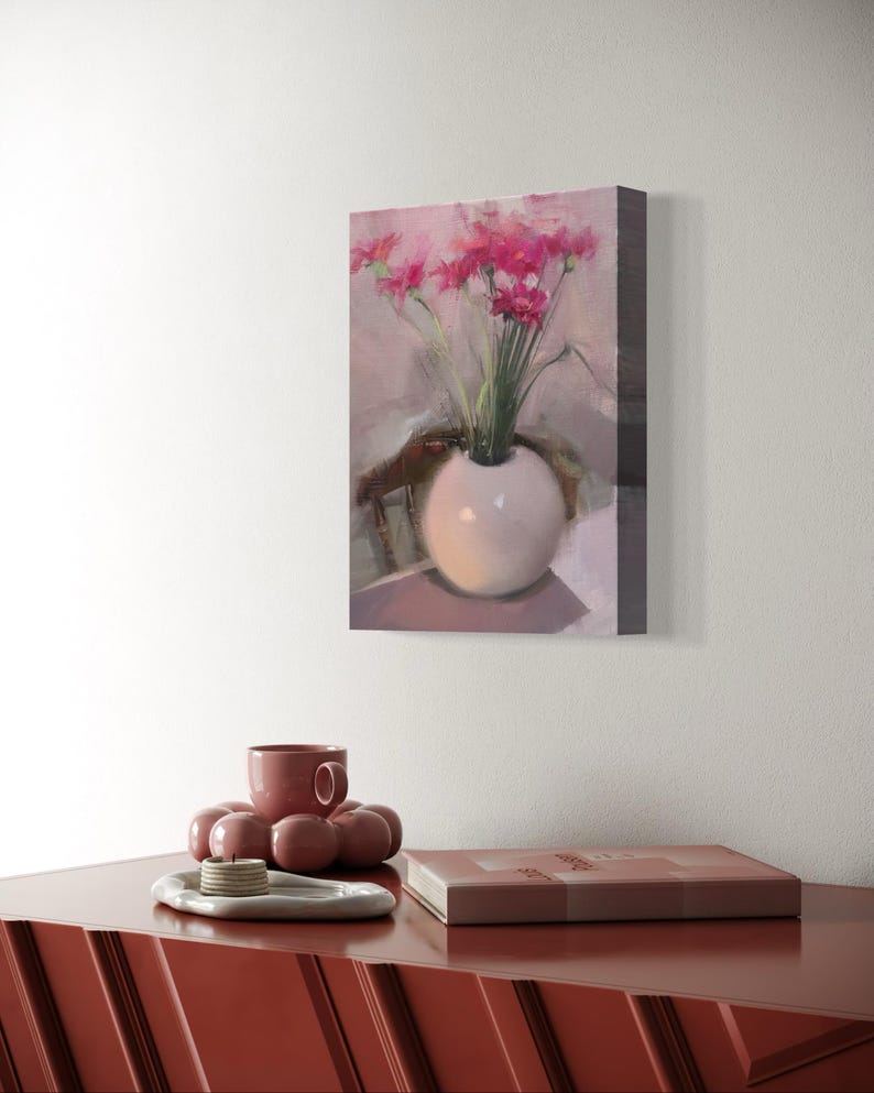 May include: A still life painting of pink flowers in a white vase. The painting is mounted on a wall above a red cabinet. A matching red cup and decorative tray are on the cabinet.
