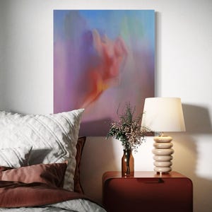 K&ouml;nnte beinhalten: Schlafzimmer-Interieur mit einem abstrakten Gem&auml;lde in Rosa-, Lila- und Blaut&ouml;nen. Ein Nachttisch mit einer Lampe und einer Blumenvase steht neben einem Bett mit Kissen und einer Bettdecke.