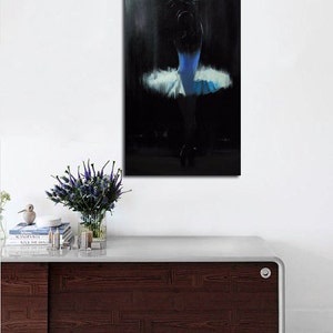 May include: An abstract painting of a ballerina in a blue and white tutu. The artwork is set against a dark background, with the dancer's form subtly illuminated. The painting is mounted on a white wall above a dark wood cabinet.