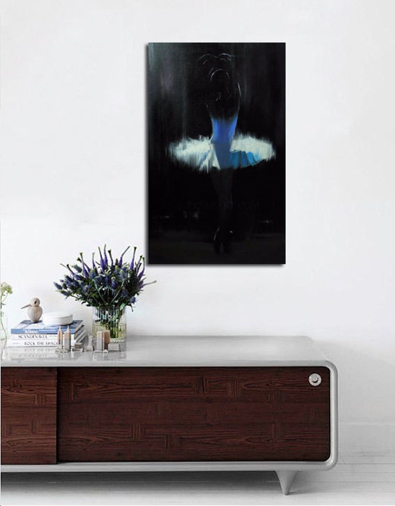 May include: An abstract painting of a ballerina in a blue and white tutu. The artwork is set against a dark background, with the dancer's form subtly illuminated. The painting is mounted on a white wall above a dark wood cabinet.