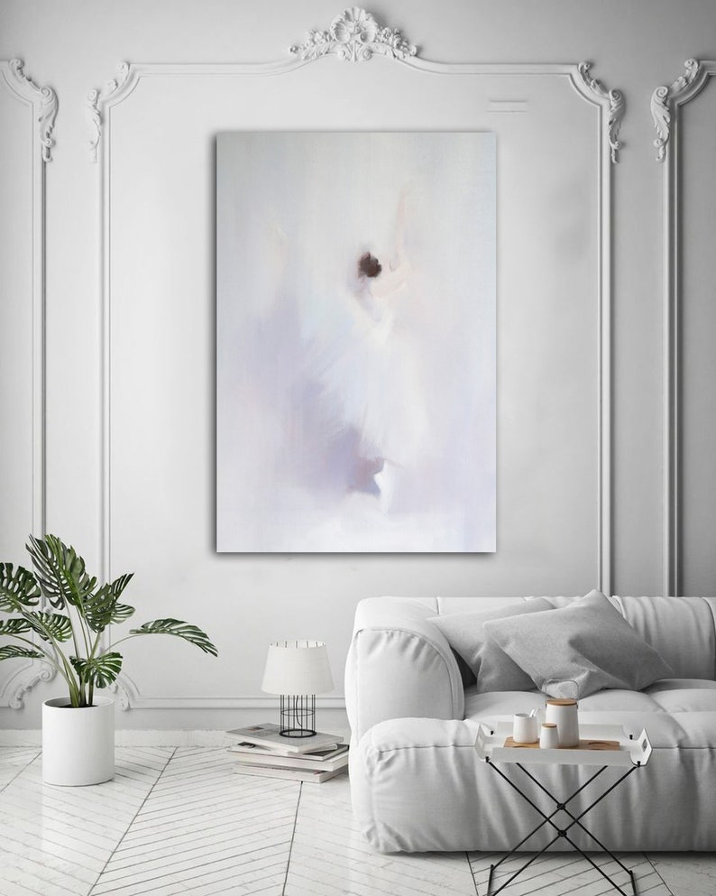 May include: An abstract painting in soft white, lavender, and brown tones hangs on a white wall. The artwork depicts a blurred figure, possibly a dancer, with a flowing white dress. The room features a white sofa, a potted plant, and a small table with decorative items.