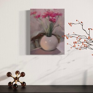 May include: An oil painting of a white vase filled with pink flowers. The vase is round and sits on a table. The painting is displayed on a white wall, with a decorative sculpture and branch with orange berries in the foreground.