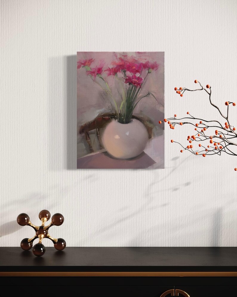 May include: An oil painting of a white vase filled with pink flowers. The vase is round and sits on a table. The painting is displayed on a white wall, with a decorative sculpture and branch with orange berries in the foreground.
